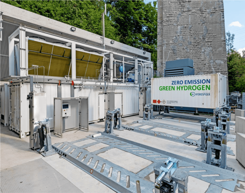 Une installation de production d'hydrogène vert avec des équipements et des conteneurs étiquetés, portant un panneau indiquant « Hydrogène vert à zéro émission » par H2 Energy.
