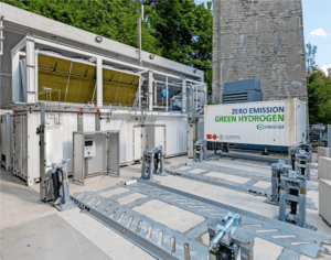 Une installation de production d'hydrogène vert avec des équipements et des conteneurs étiquetés, portant un panneau indiquant « Hydrogène vert à zéro émission » par H2 Energy.