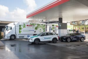Deux voitures à hydrogène font le plein dans une station d'hydrogène, avec un camion de livraison d'hydrogène garé à proximité sous un auvent de carburant.