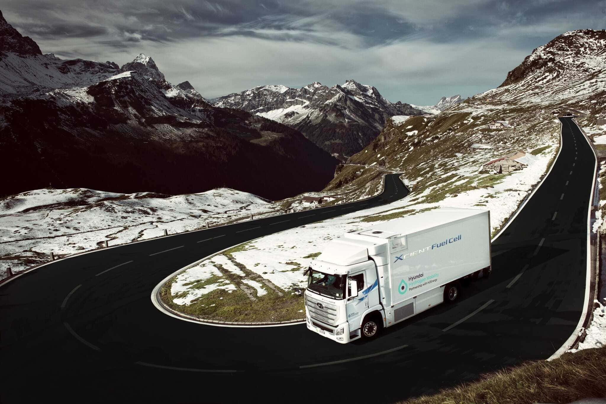 Un camion blanc à pile à hydrogène roule sur une route de montagne sinueuse avec, en arrière-plan, des pentes enneigées et des sommets imposants.