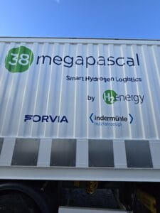 A white truck container displays the text "38 megapascal Smart Hydrogen Logistics by H2energy" along with Forvia and Indermühle logos against a clear blue sky.