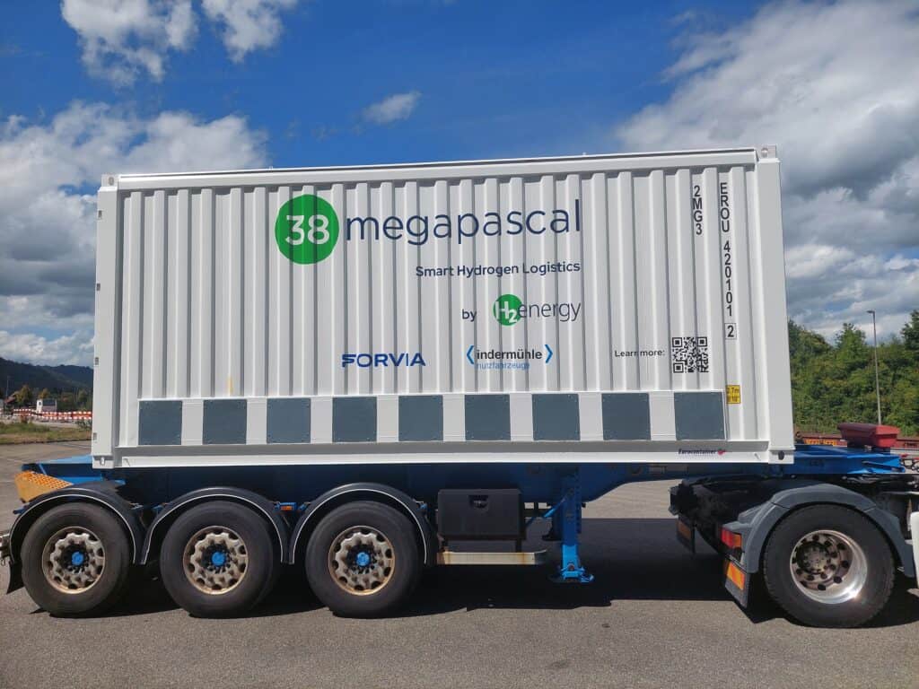A trailer holds a white container labeled "38 megapascal Smart Hydrogen Logistics by H2energy" with company logos and a QR code on its side.